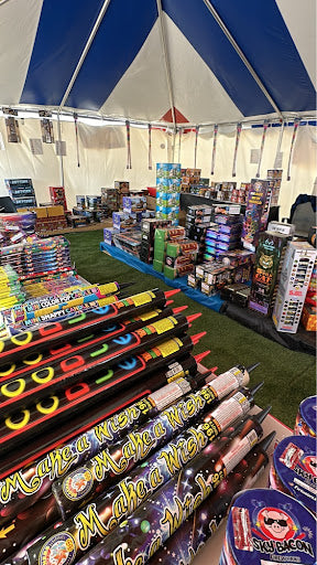 Display of fireworks under a blue and white tent with various types of fireworks on display.